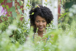 A woman standing in a plant nursery, surrounded by plants, flowers and foliage.