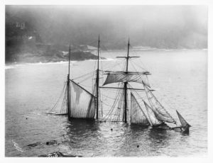 A starboard bow view of the three-masted barquentine Mildred (1889) submerged with just the masts above water, taken from the cliffs.