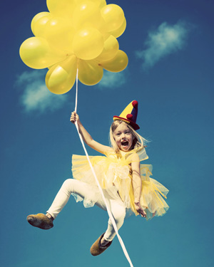 A smiling little girl holds on two a bunch of yellow balloons