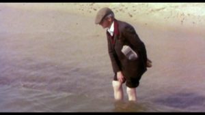 Man in a flat cap wading in the sea