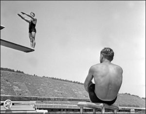 Man watching a high diver preparing to jump from diving board. Date: 1930s