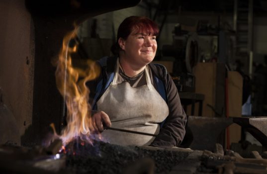 A female steel worker sat by a forge