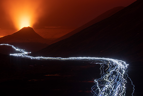Long line of people, mainly local, walking with headlights, heading back from a visit to the Fagradalsfjall volcano, Iceland. Long exposure showing direction of movement. 2 April 2021