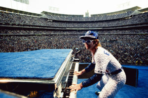 English singer songwriter Elton John performing at Dodger Stadium in Los Angeles, October 1975. He is wearing a sequinned baseball outfit.