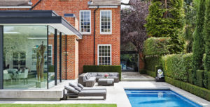 Exterior of house with dining room extension with glass wall, bespoke lap pool, a lawn and sun loungers